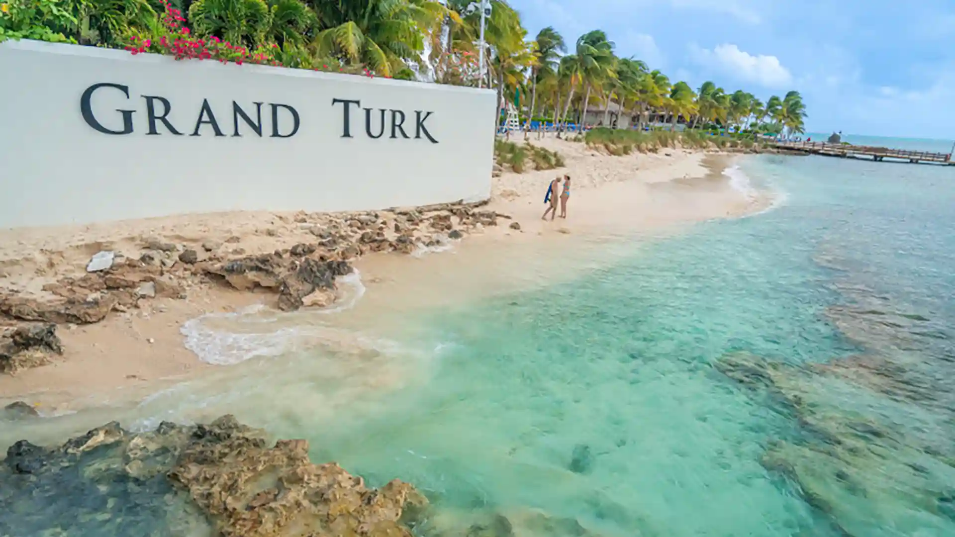 View of Grand Turk sign near beach with palm trees in background.