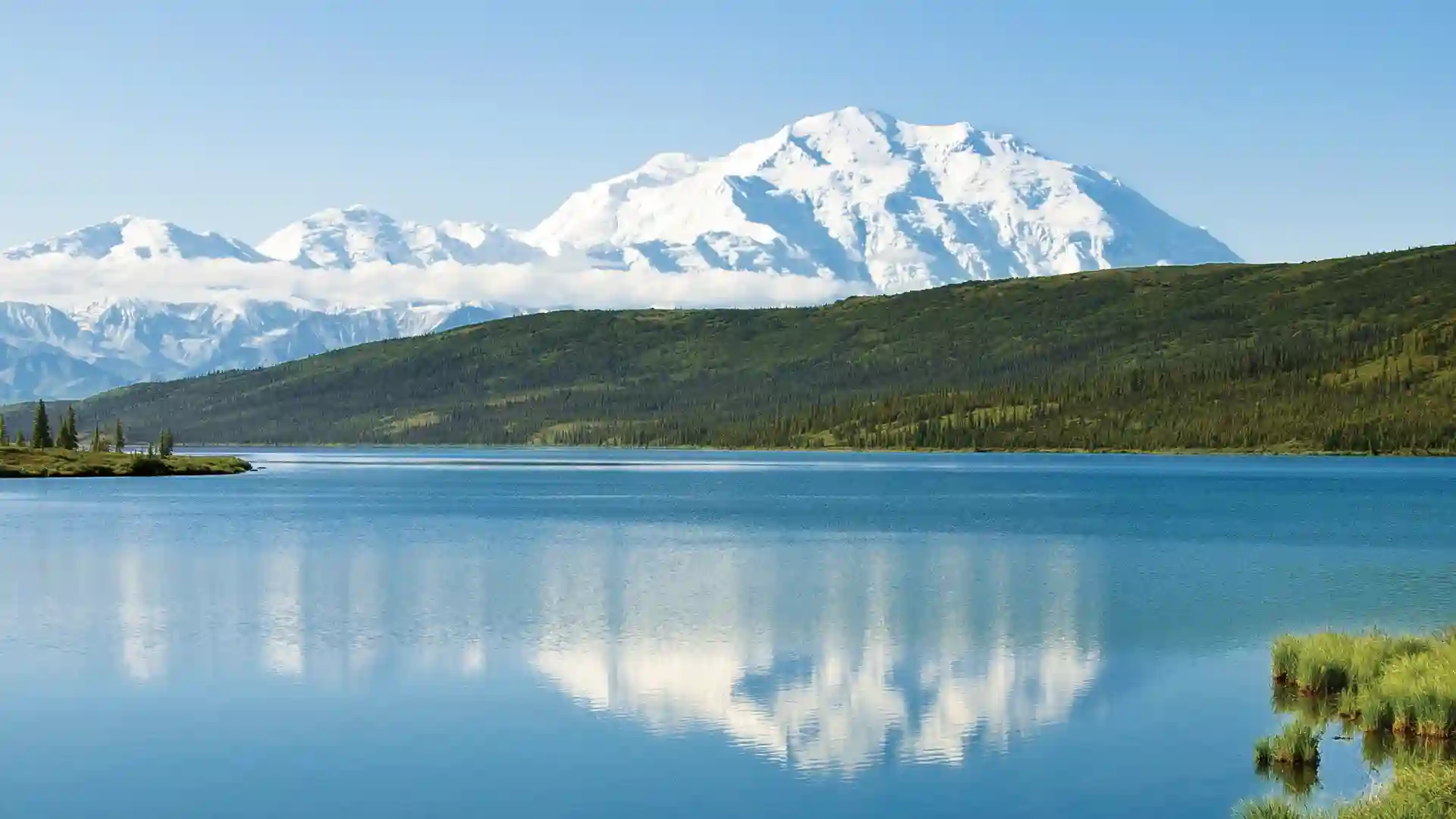 View of snowcapped mountains, green landscape and calm water reflecting the mountain range in Denali National Park.