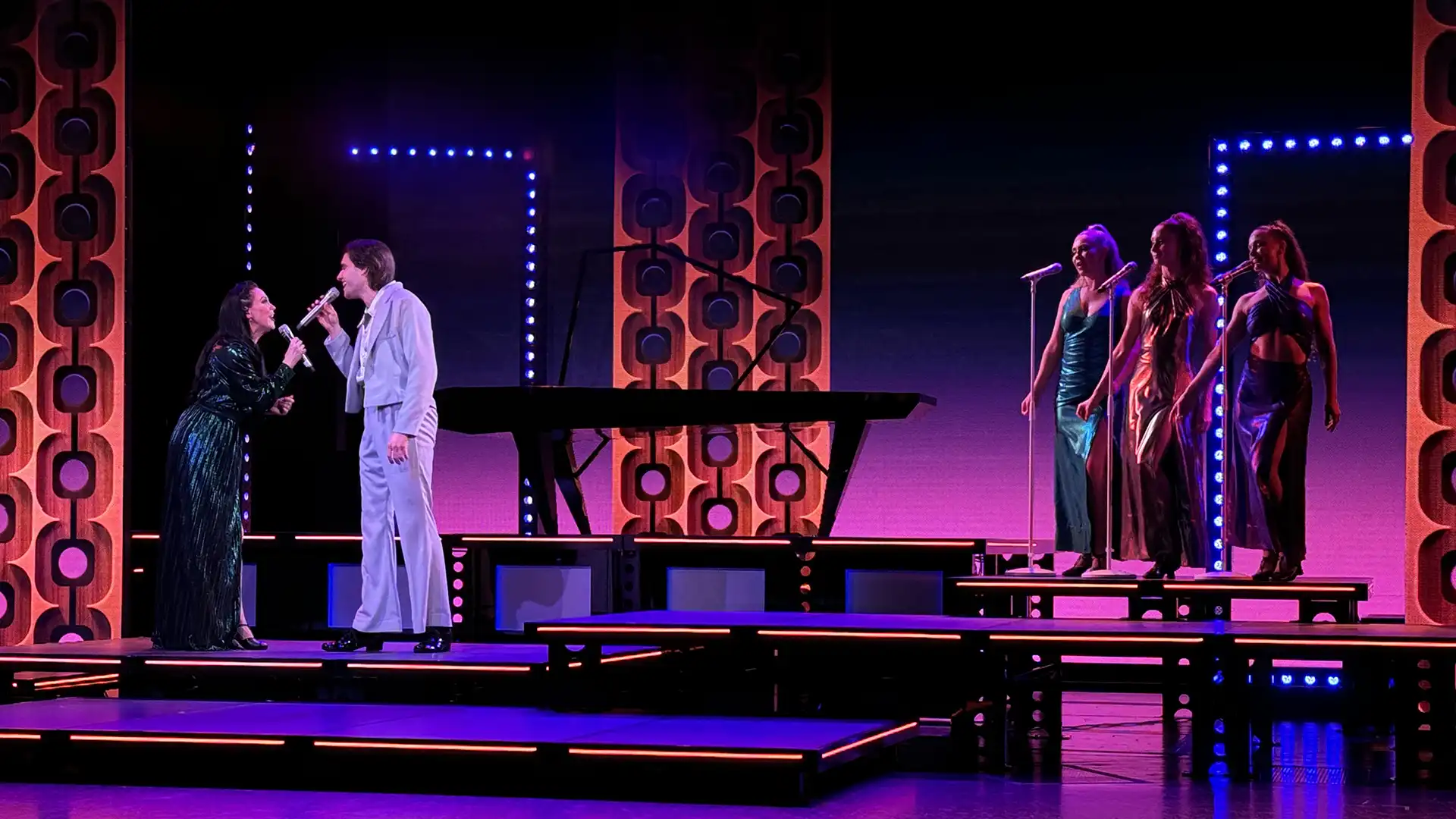 View of Holland America Line performers singing on stage with multicolored lighting in background.