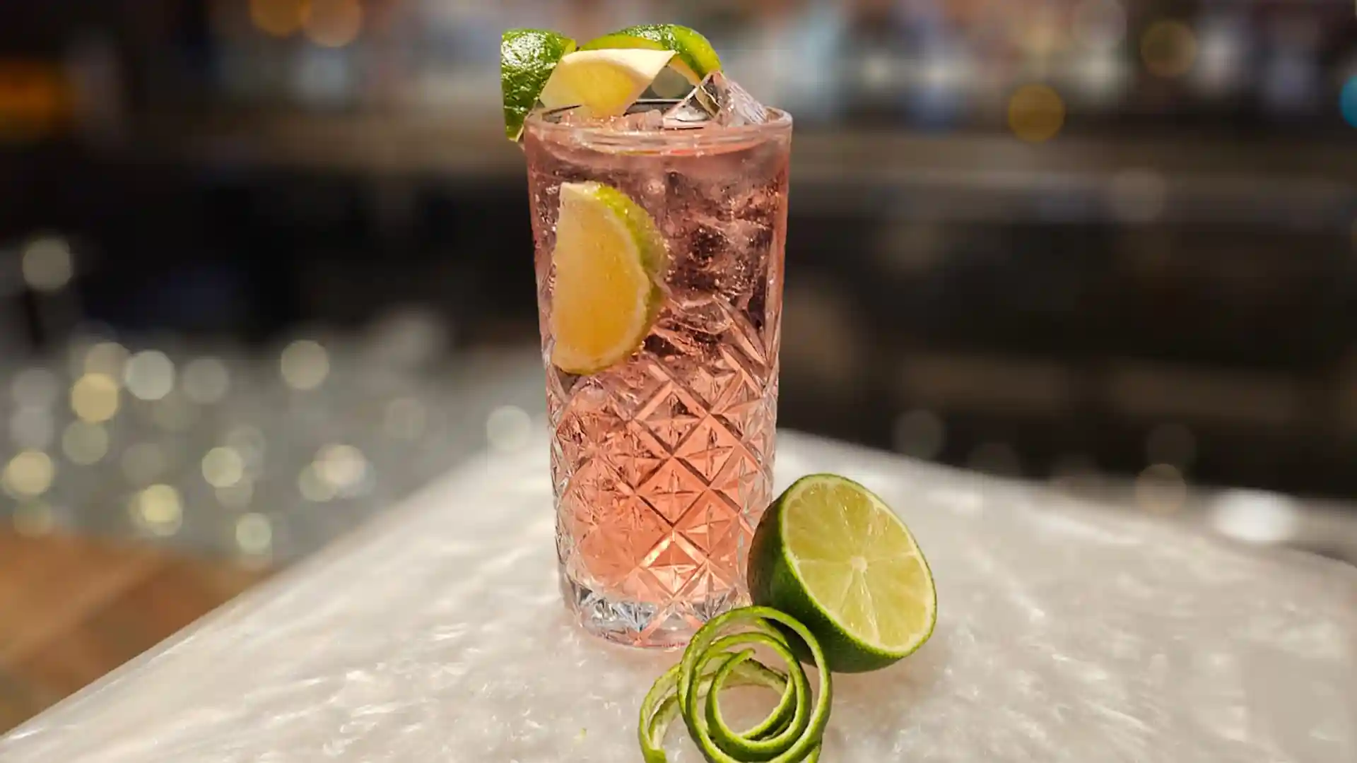View of pink-colored cocktail with lime garnish.