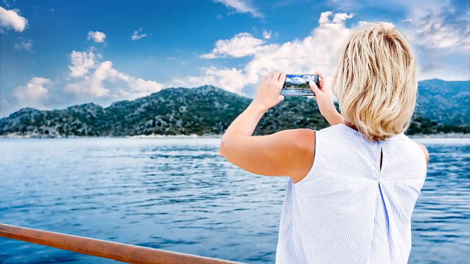 View of person taking photos of landscape from deck of cruise ship.