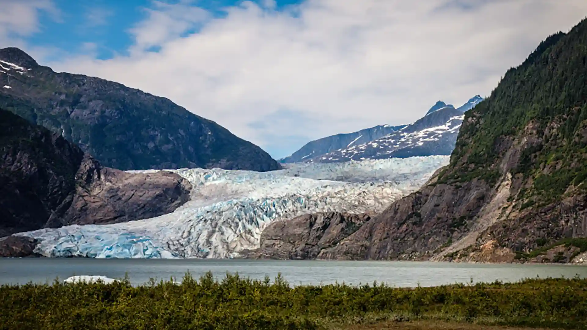 View of Mendenhall Glacier in Alaska, surrounded by rocky mountains covered in forest and snow.