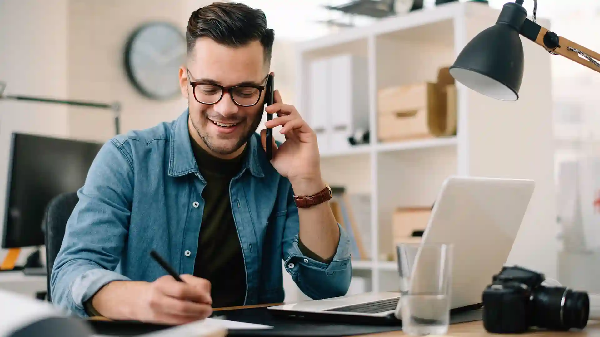 View of person on phone writing notes at desk.