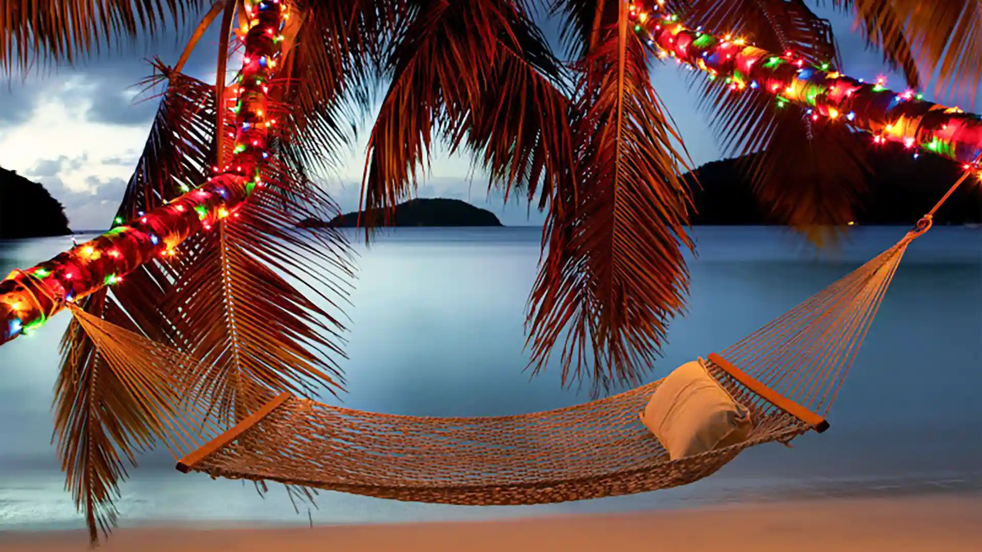 Holiday Vacation at the Beach Hammock on beach below multicolored holiday lights with ocean in background.