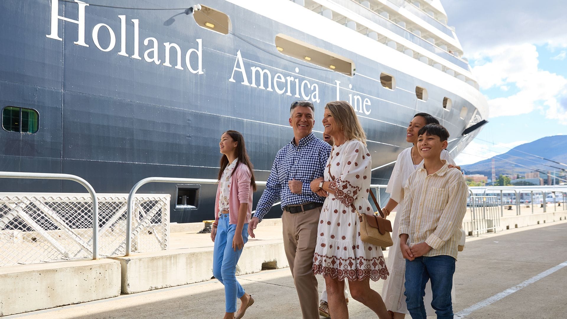 A group of five people, three adults and two teenagers walking in front of a Holland America cruise ship.