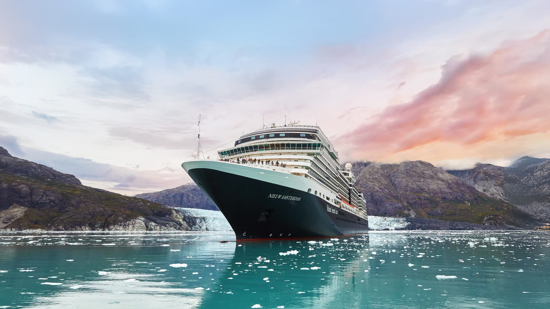 061025_SEO Blog_The Best Time to Cruise to AK_Ship in Summer Holland America Alaska cruise ship on blue water with snow-capped mountains and a blush-colored sunset in the background.