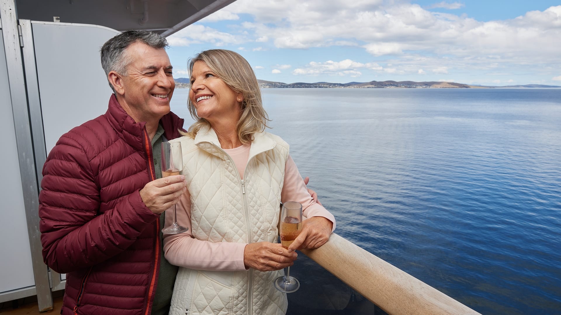 Couple enjoying champagne on the deck of a cruise ship with calm water behind them.
