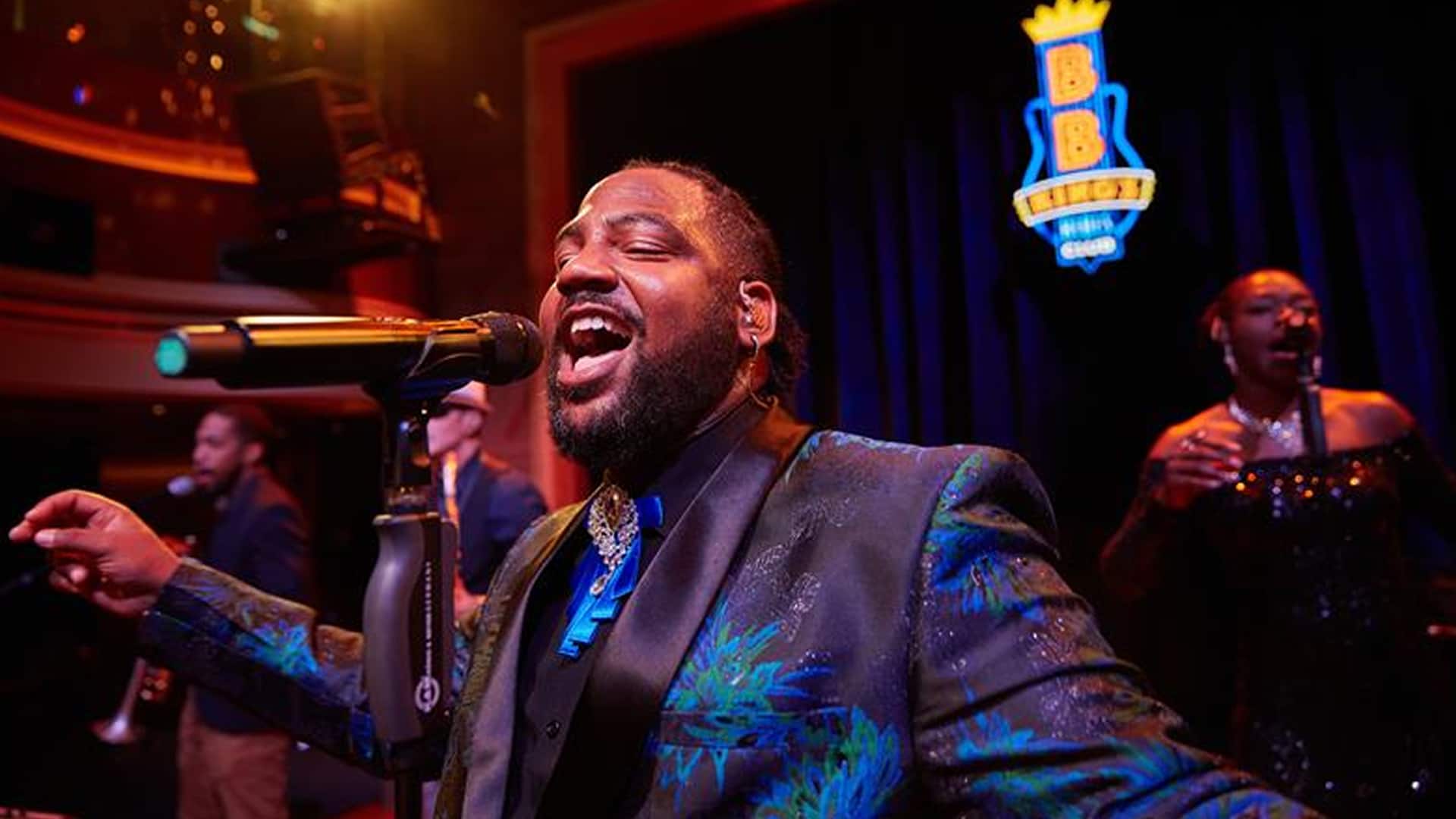 A performer singing in the mic with the BB Kings Blues Club sign in the background and other.