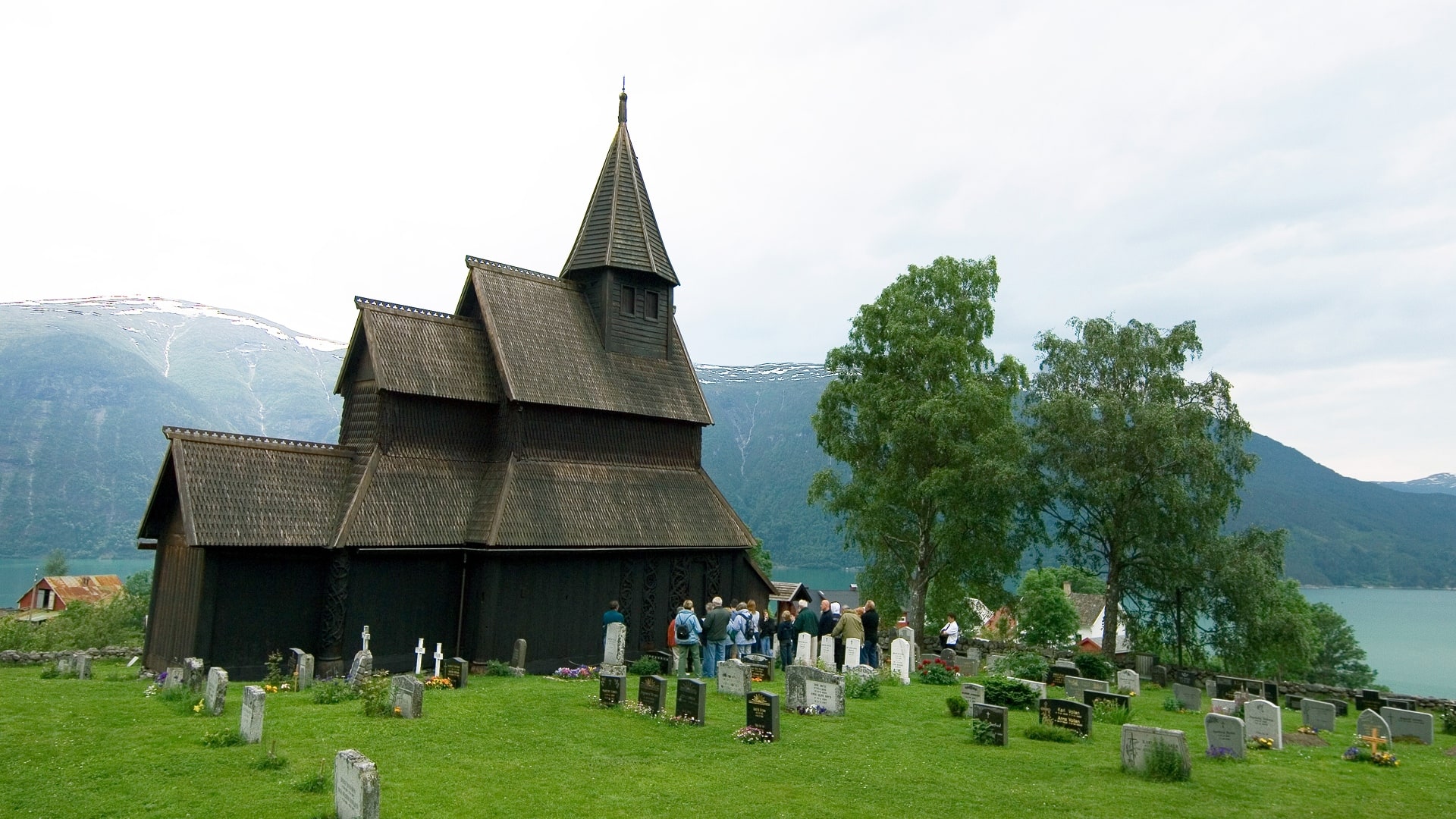 A group of people in Urnes, Norway, taking a tour of Urnes Stave Church and its Viking graveyard.