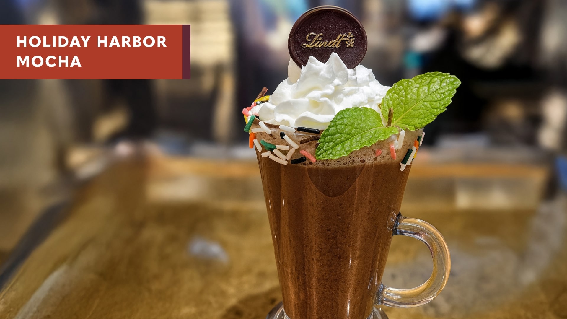 Holiday harbor mocha, in a tall glass with sprinkles around the rim & whipped cream.