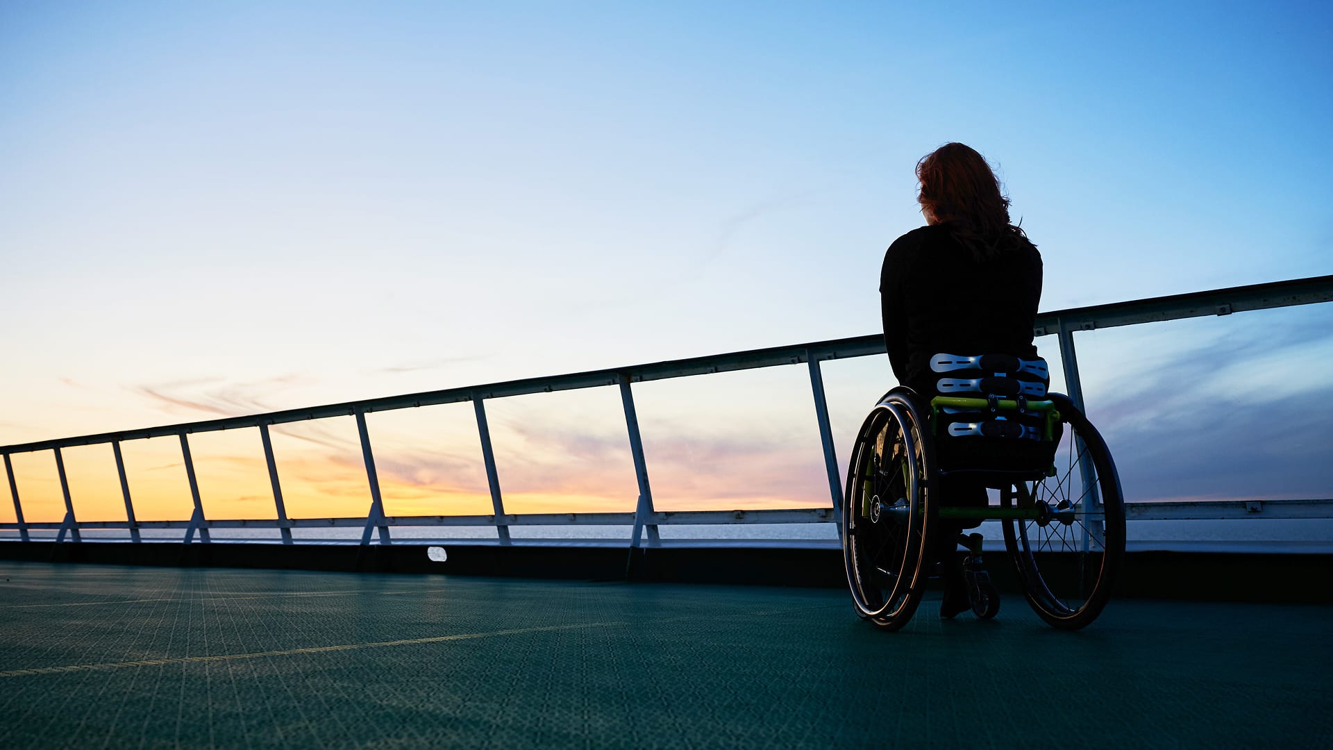 A person who uses a wheelchair watching the sunset from the deck of a cruise ship.