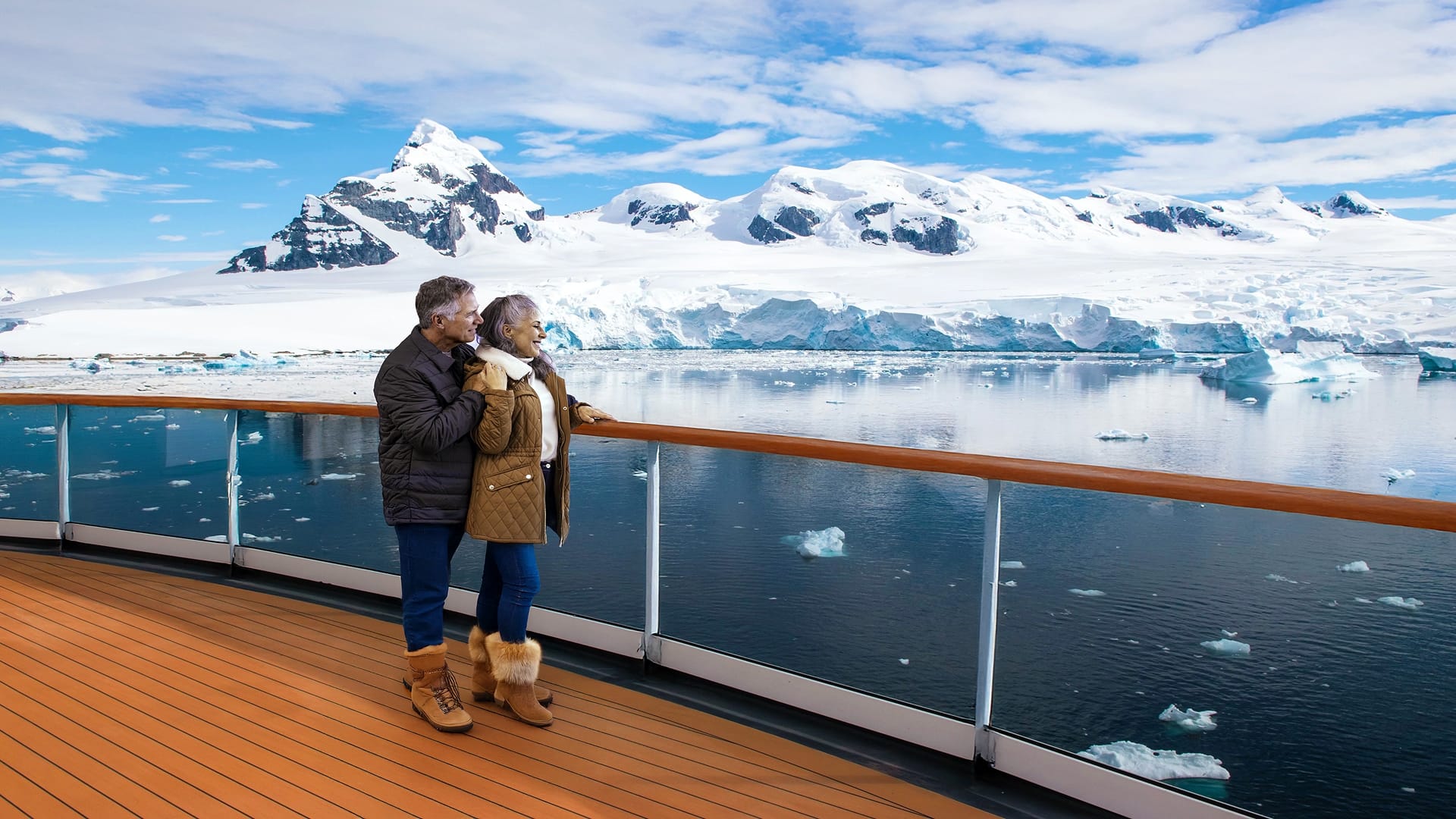 Two people on a ship deck holding glasses of champagne with the ocean in the background.