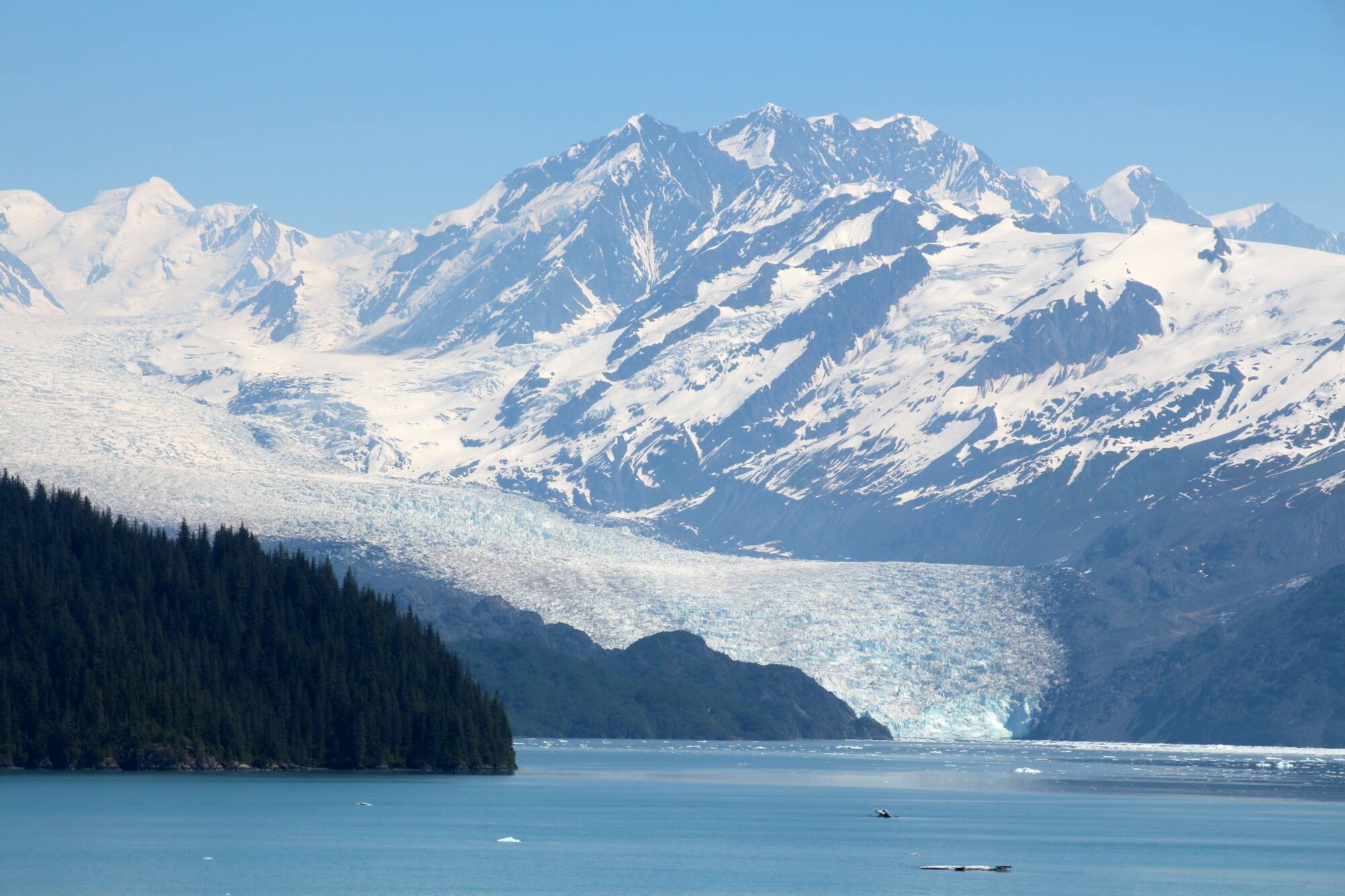 Glacier descending into a bay with mountain peaks in the background.