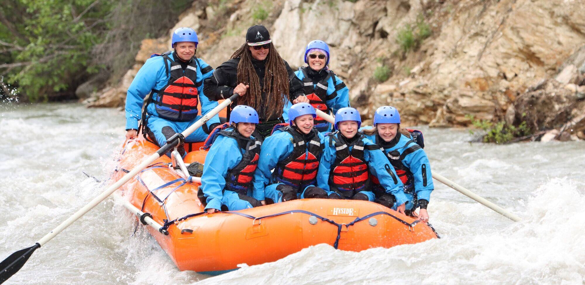 Group navigating whitewater rapids in an orange rafting boat.