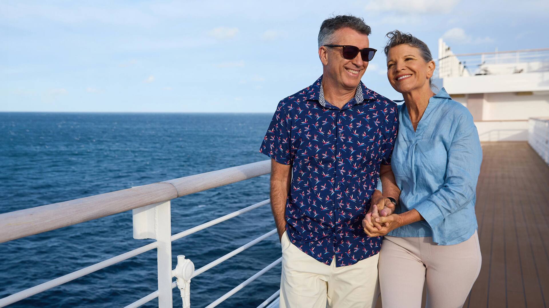 A smiling couple holding hands on the deck of a cruise ship.