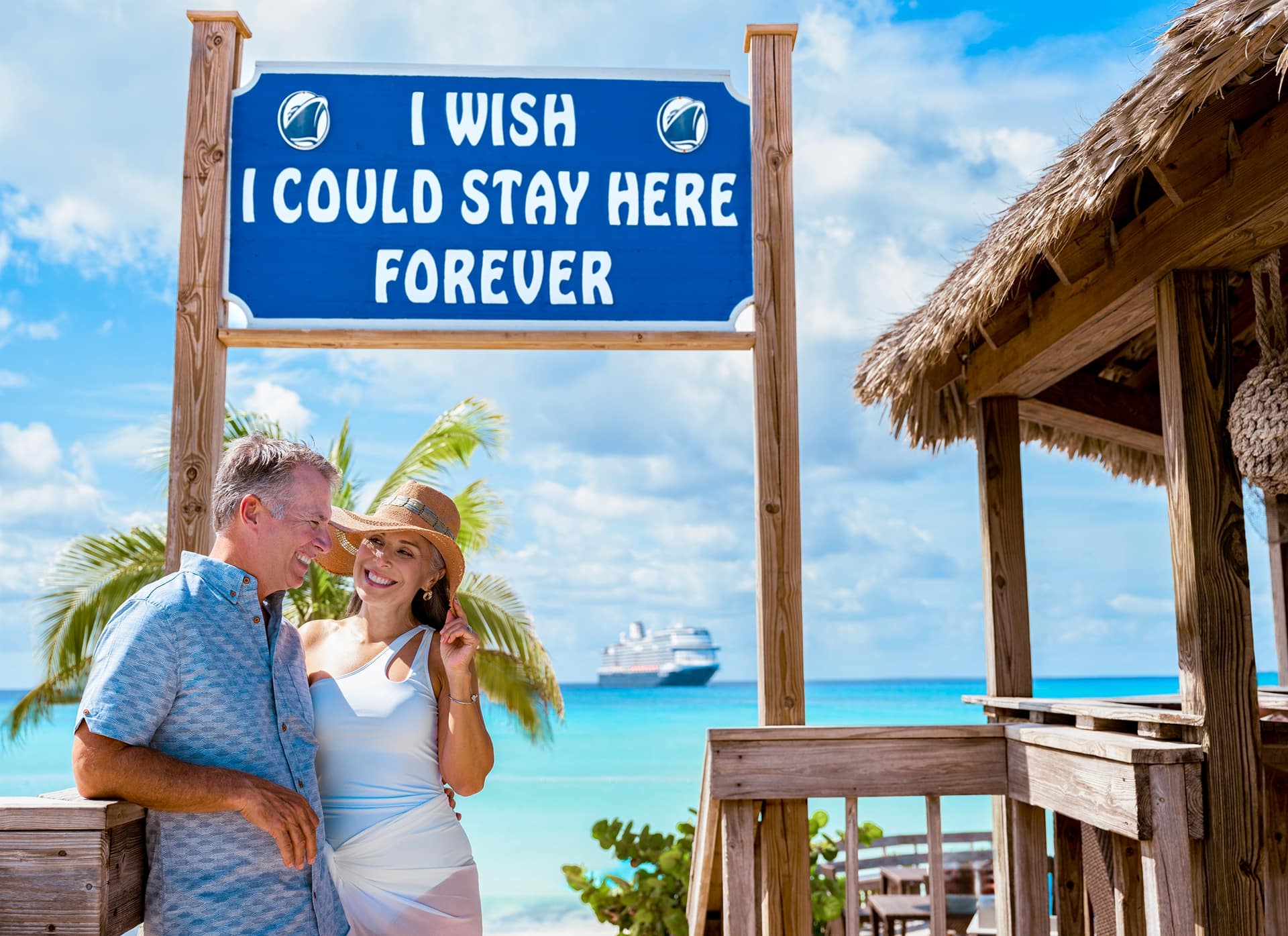 A woman and a man in front of a sign at RelaxAway,Half Moon Cay with the text I Wish I Could Stay Here Forever.