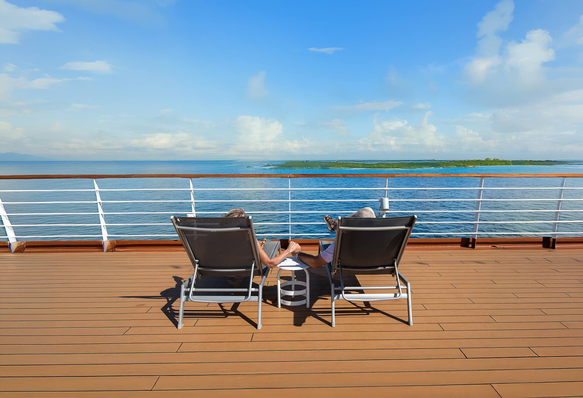 A couple sitting in gray chairs on the deck of a Holland America ship in the Caribbean.