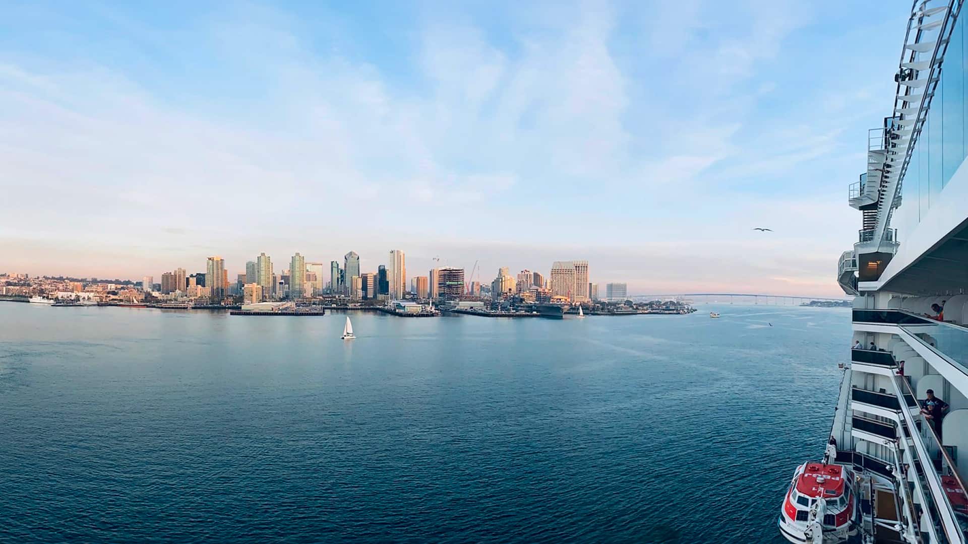 The San Diego skyline in the distance with a cruise ship side panel, red lifeboat, and balconies.