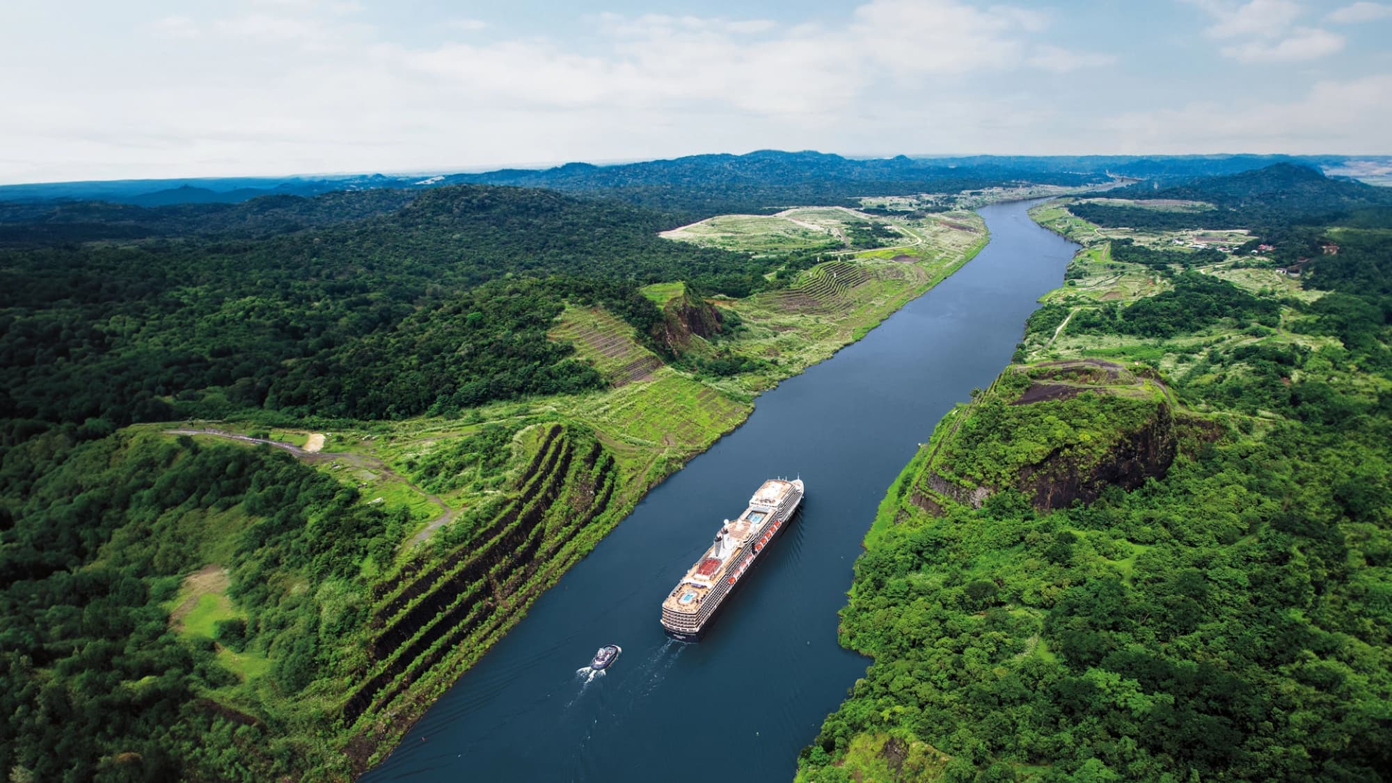 Holland America cruise ship moving through the narrow Panama Canal flanked by green jungle foliage on each side.