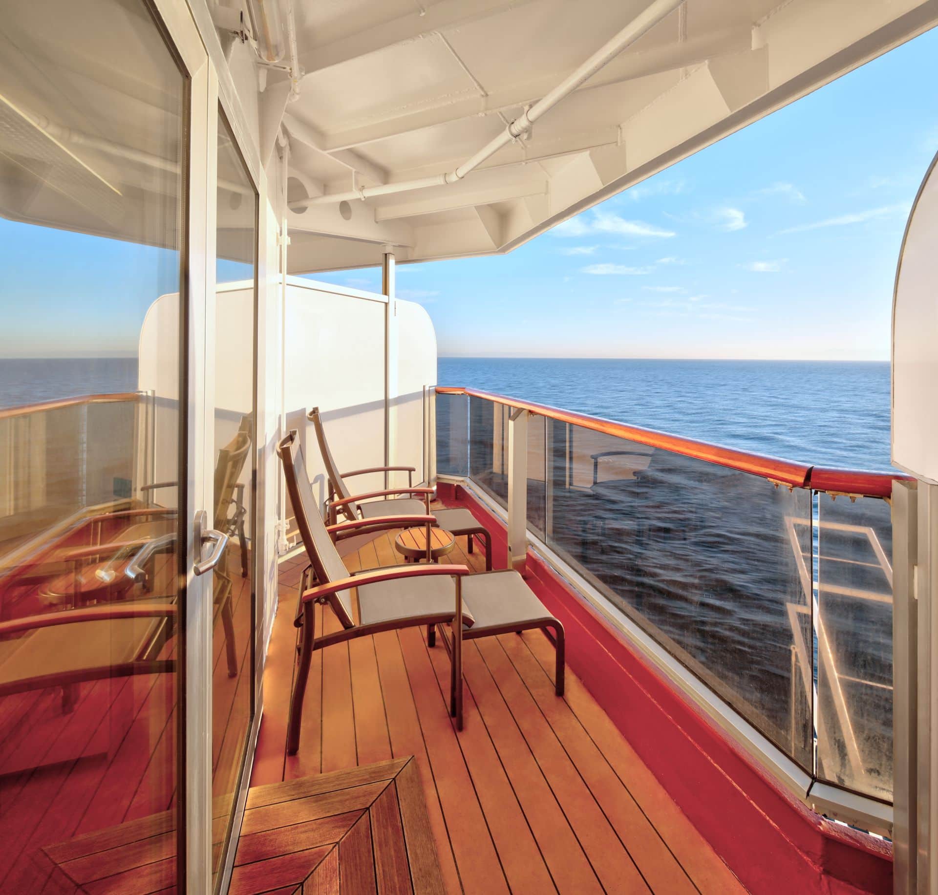 Cruise ship balcony with two chairs, small table, glass railing, and ocean view.