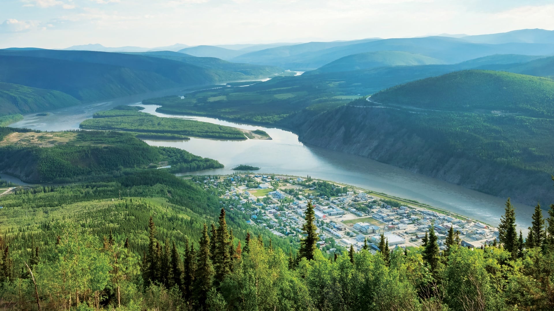 Aerial view of a winding river flowing through forested mountains, with a small town nestled along the riverbank.