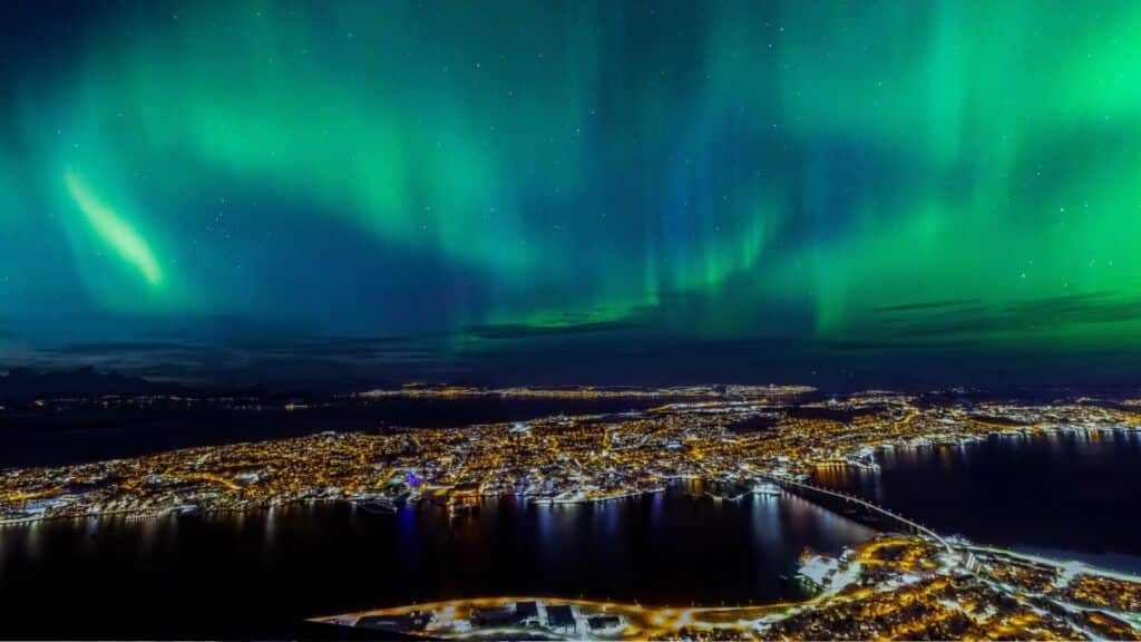 Green Northern Lights, one of the highlights of Europe in fall, winter, and early spring, fill the night sky over a city in Norway.