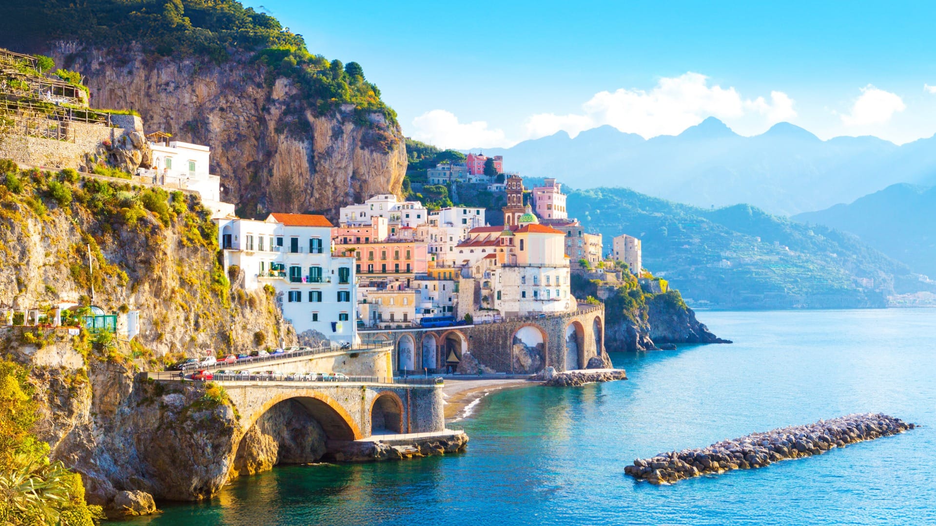 collector-voyages-blog-header Coastal village built into seaside cliffs overlooking a calm blue bay and distant mountains.