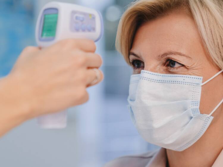 woman wearing mask having her temperature taken