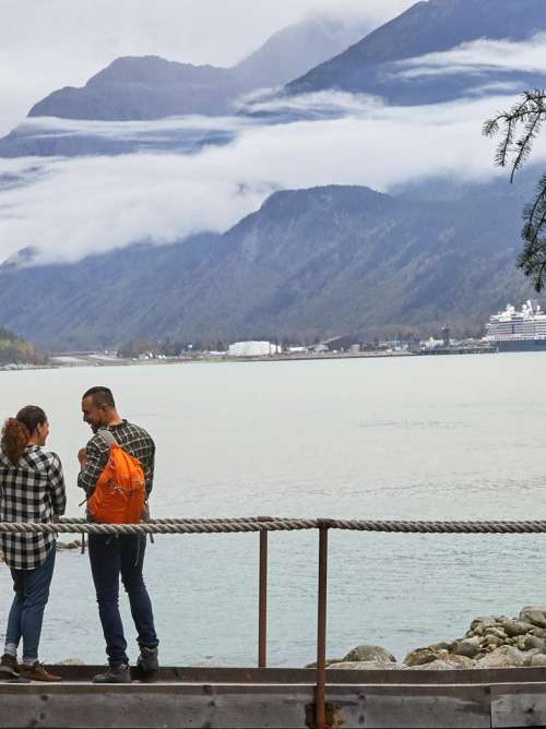 Two hikers on a bridge looking at a port in Alaska.