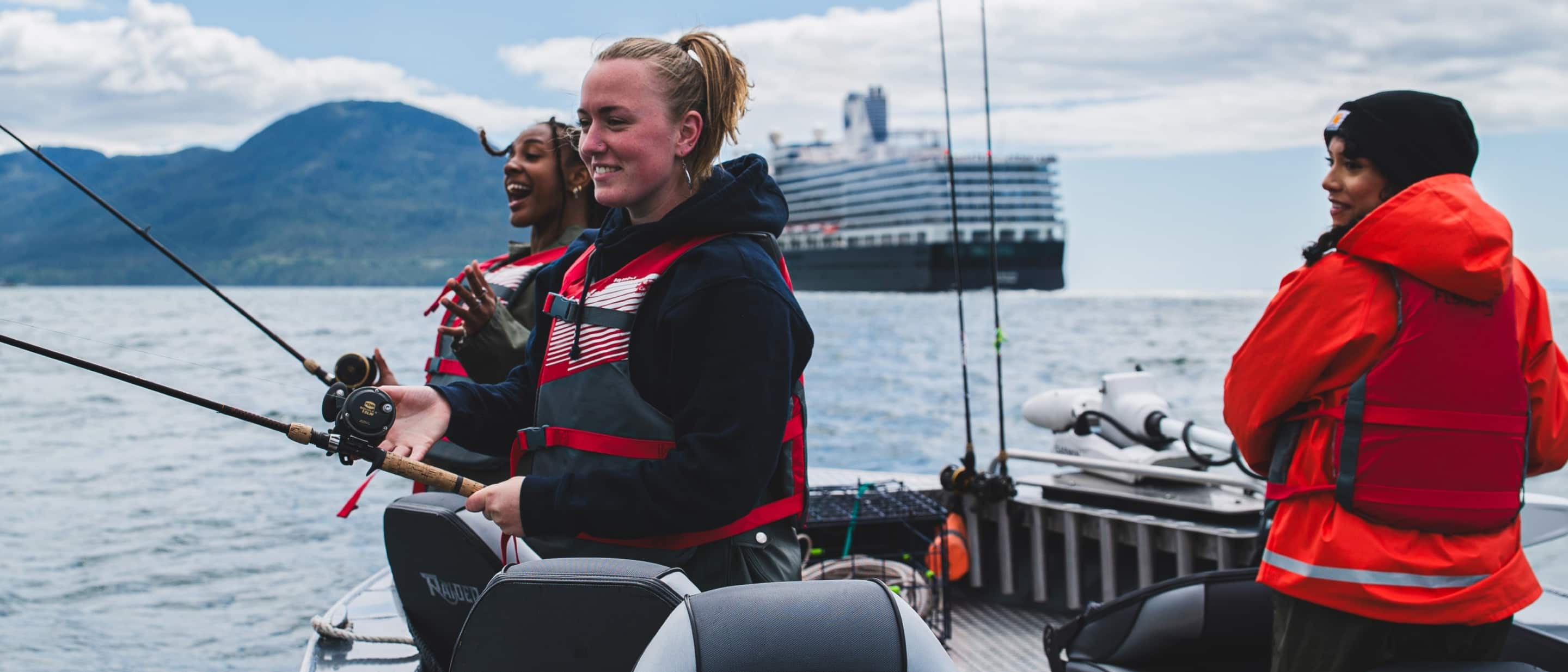 People fishing from a boat on the ocean with mountains in the background and a Holland America cruise ship anchored nearby.