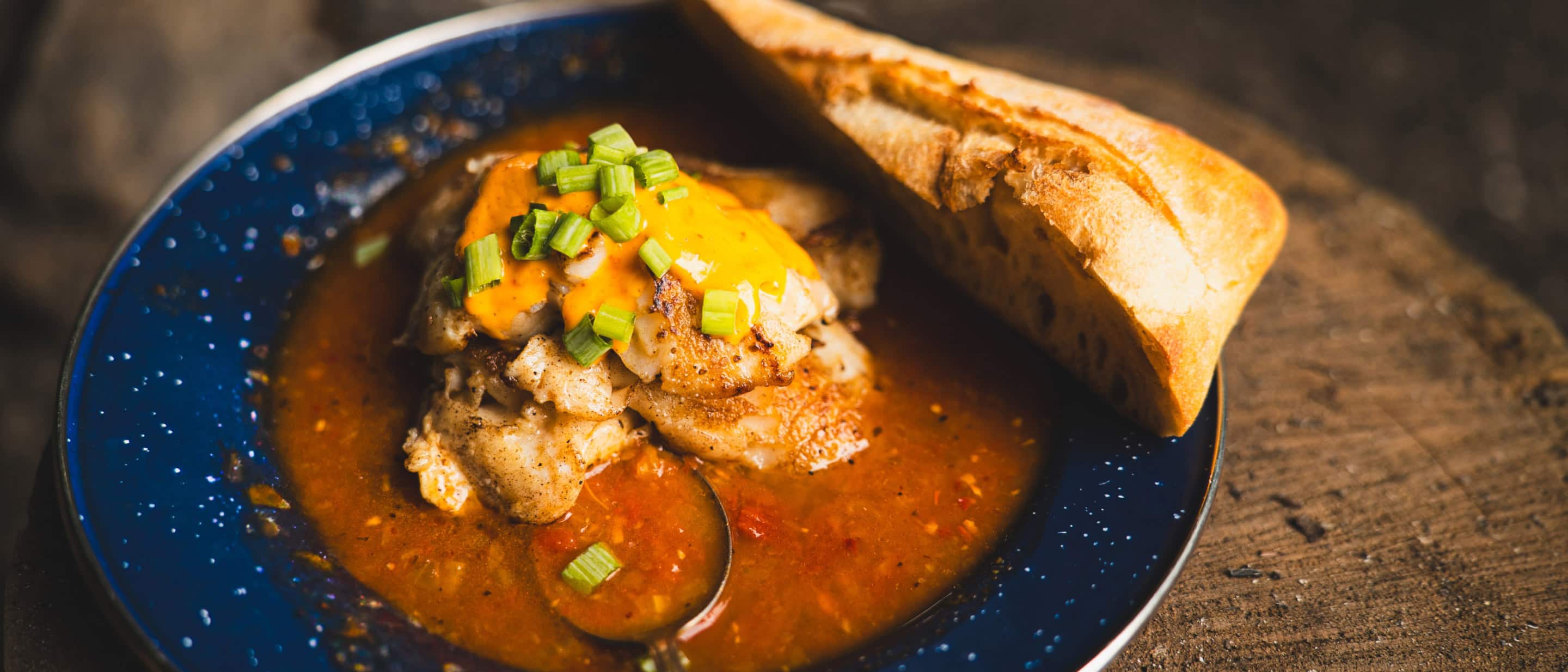 Bowl of hearty fish stew with grilled fish, spicy tomato broth, green onions, and crusty bread.