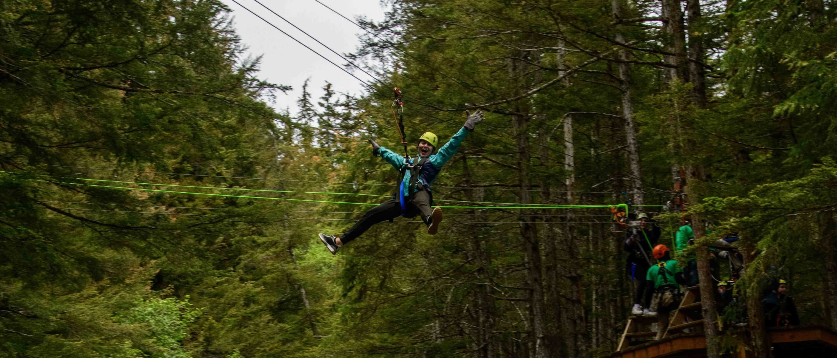 Person ziplining through a dense green forest on an adventure course with safety gear.