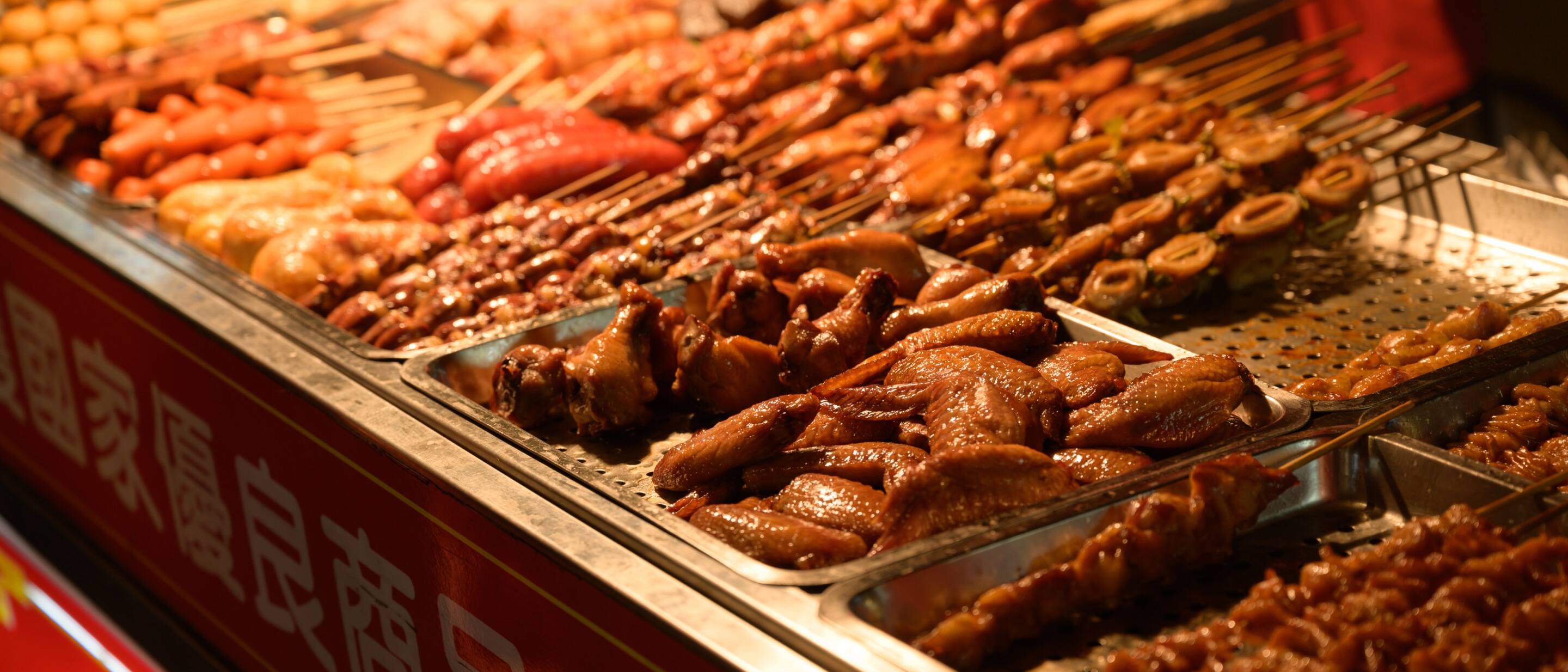 Grilled meats and skewers displayed at a bustling Kowloon street food market in Hong Kong.