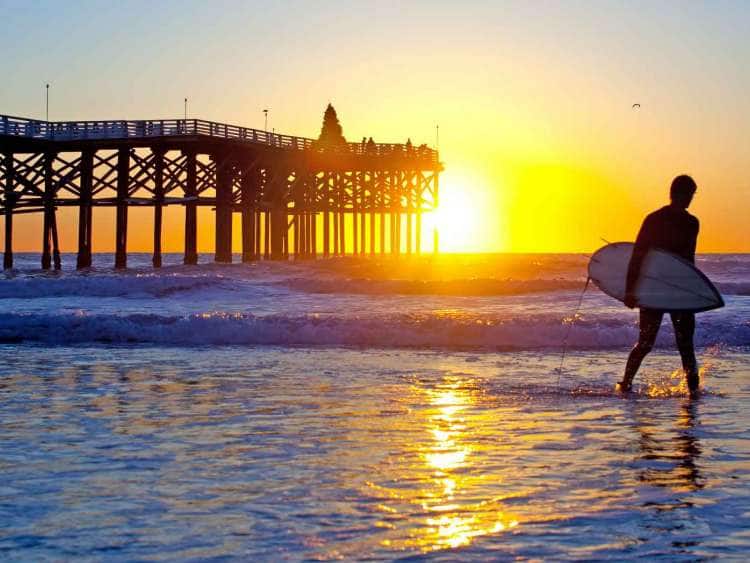 Surfer walking along California beach at sunset