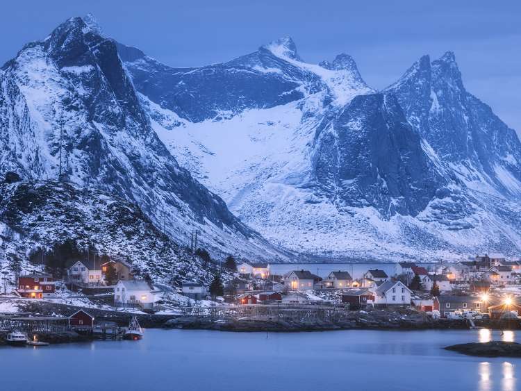 Landscape of a village with snowy mountains and lights reflected in the water