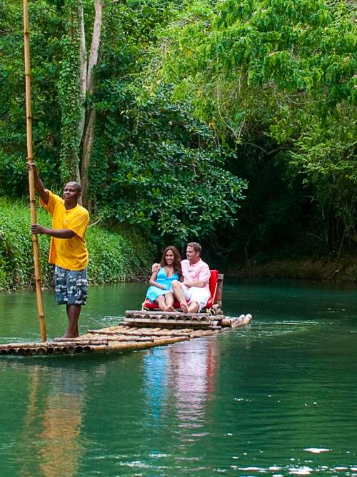 A raftsman steering a bamboo river raft with a couple sitting in the back on a tour of the Martha Brae