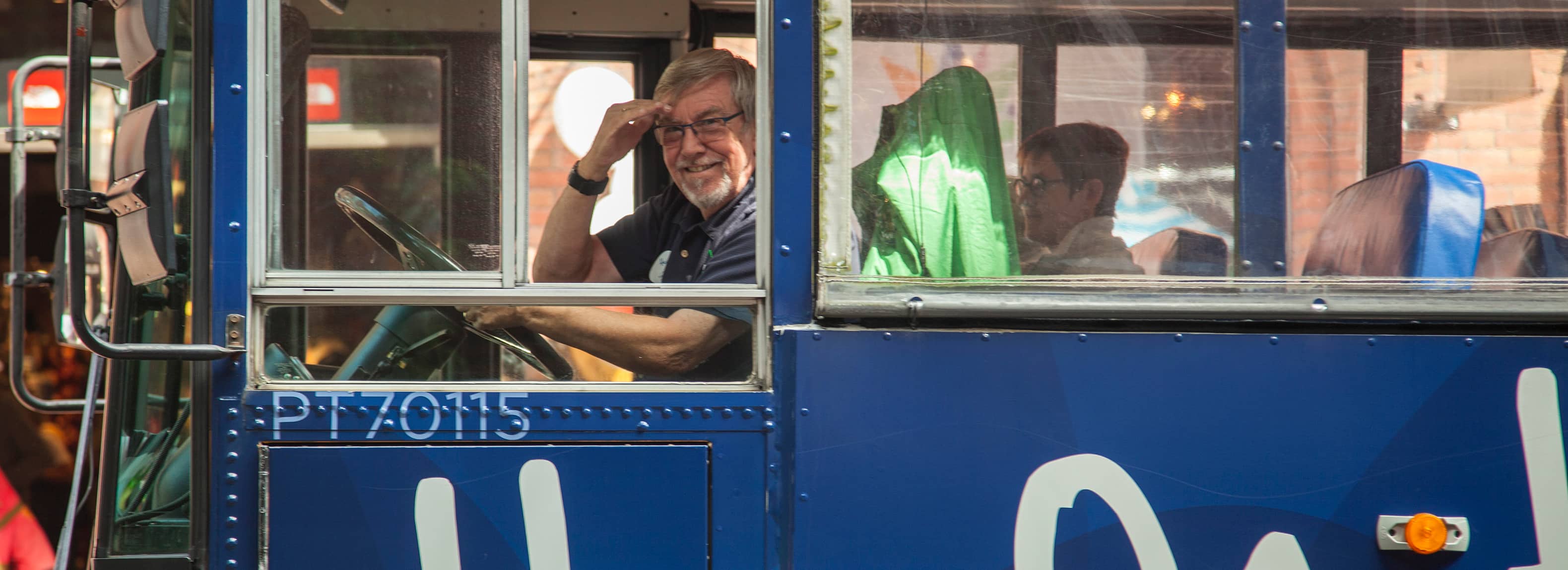 Man saluting driving a blue bus.