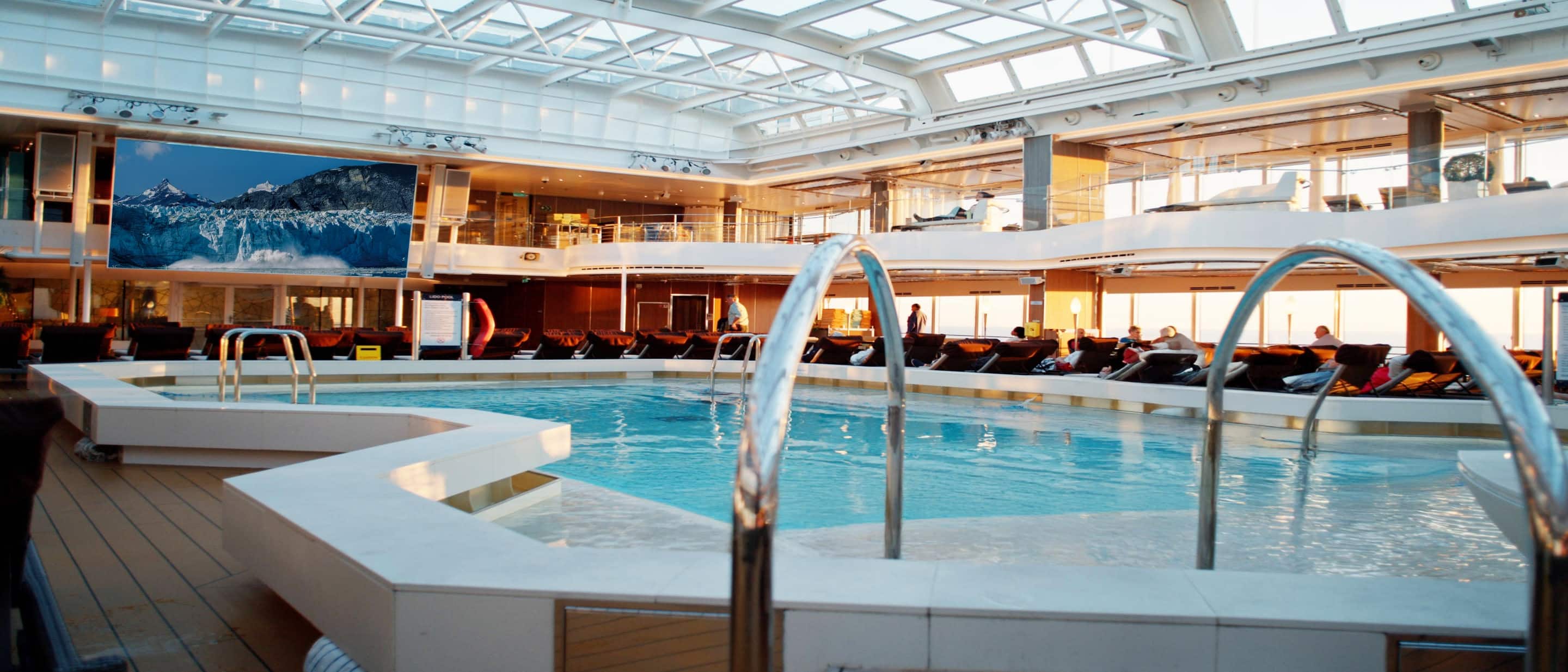 Lido Pool on Holland America cruise ship with spacious deck, loungers, and glass roof for all-weather swimming.