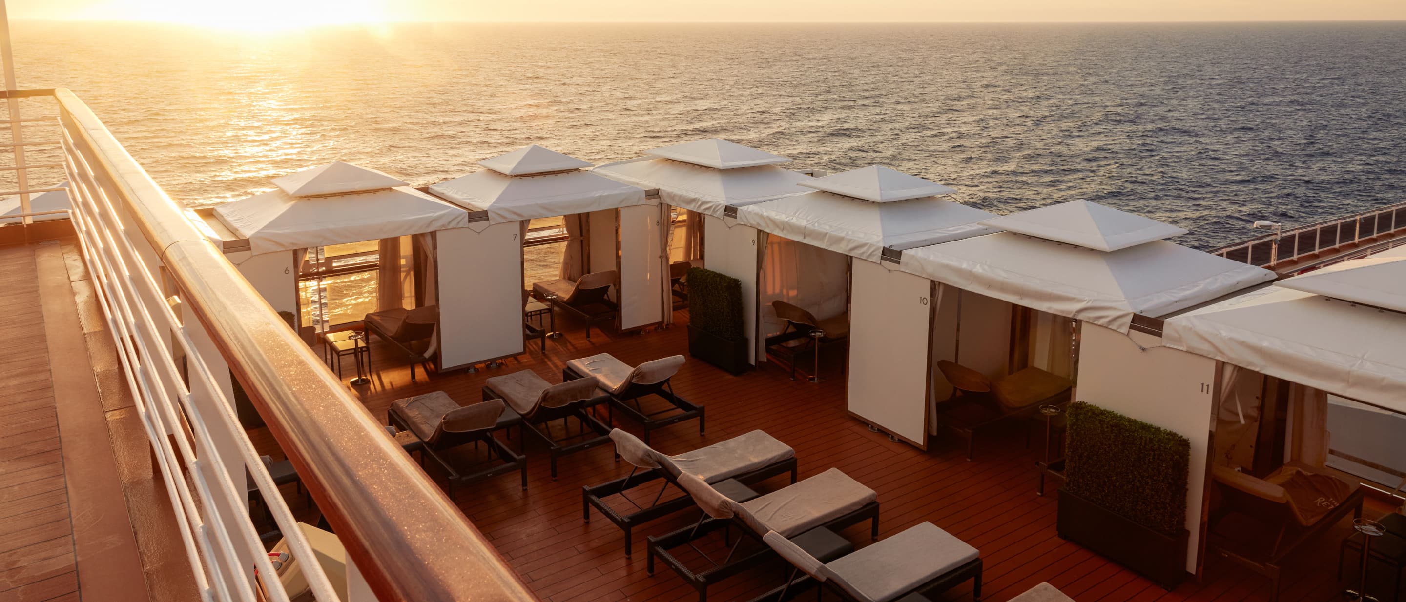 The Retreat with modern lounge chairs and cabanas at sunset on a Holland America cruise ship deck.