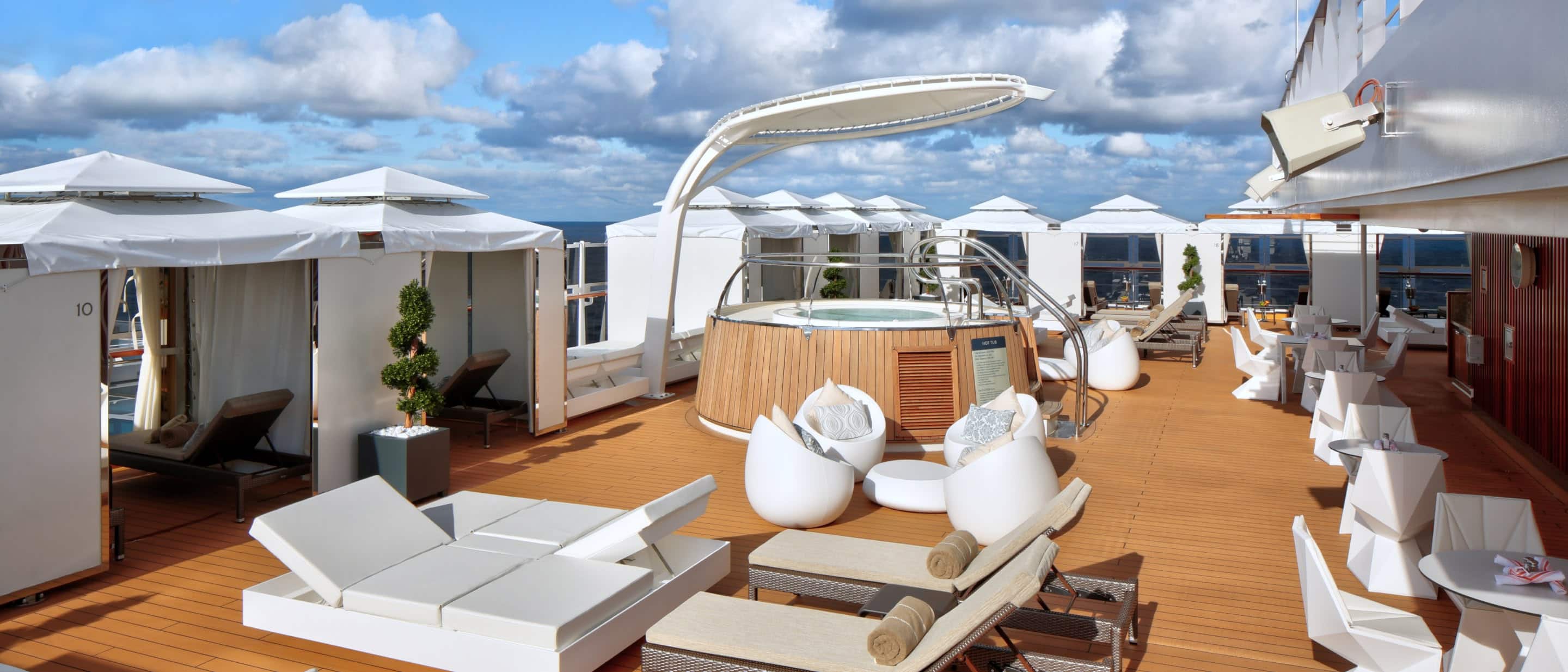 The Retreat with modern lounge chairs and cabanas under a bright blue sky on a Holland America cruise ship deck.