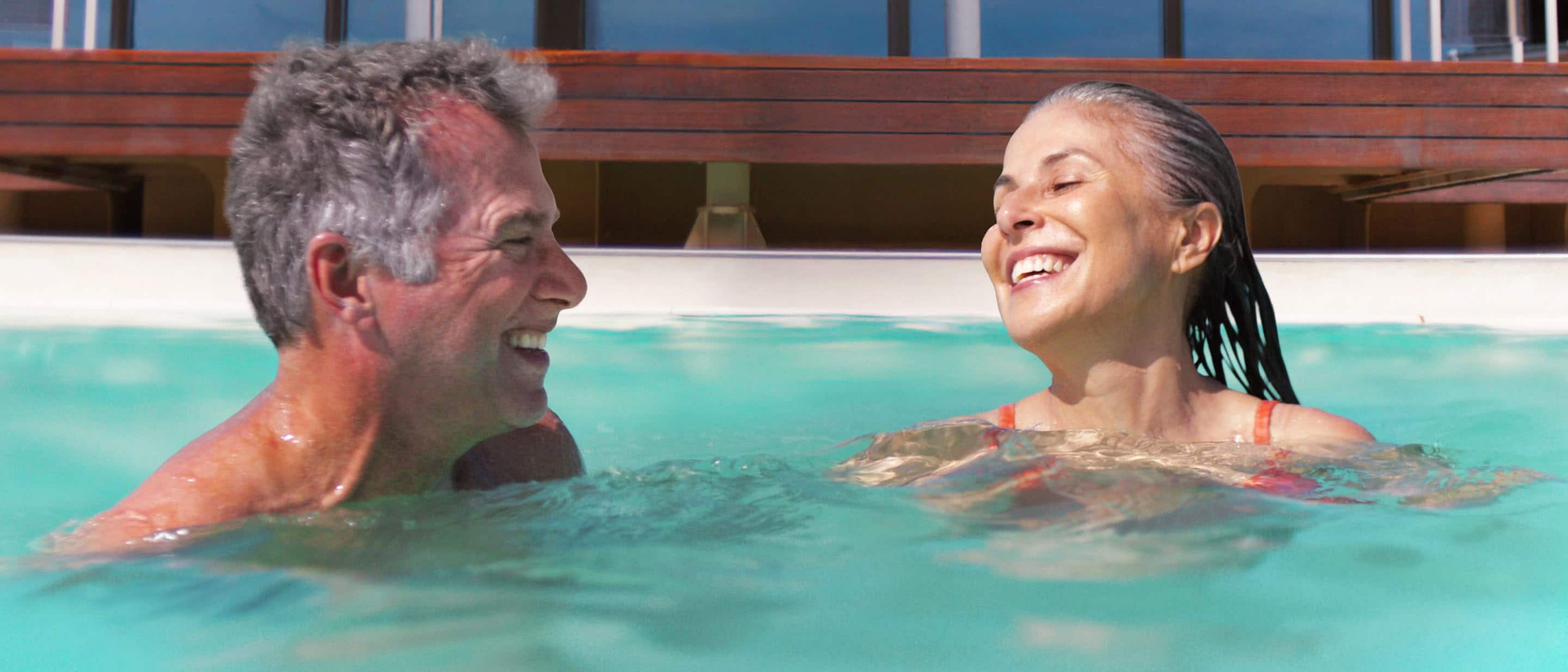 Two people in a Holland America ship’s hot tub surrounded by shimmering blue water and wooden deck.