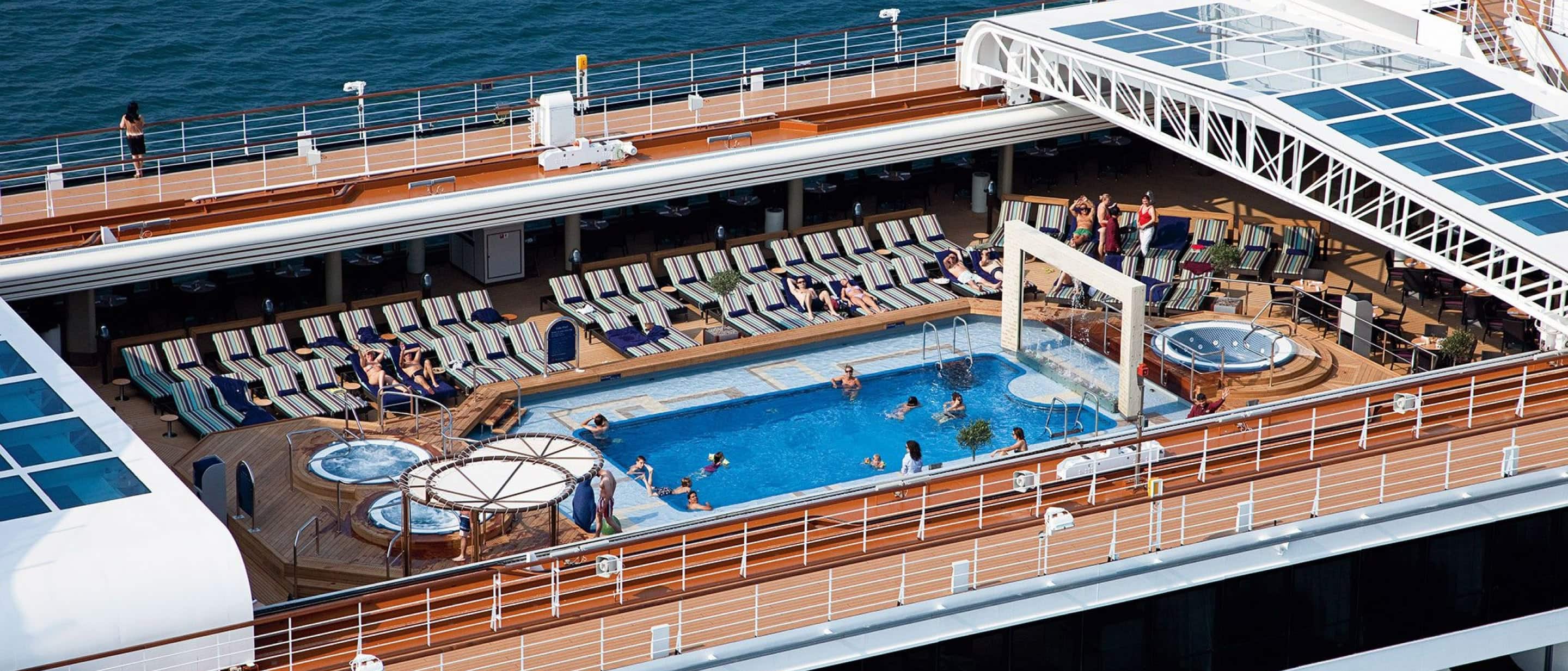 Aerial view of Lido Pool on Holland America cruise ship with spacious deck, loungers, and glass roof for all-weather swimming.
