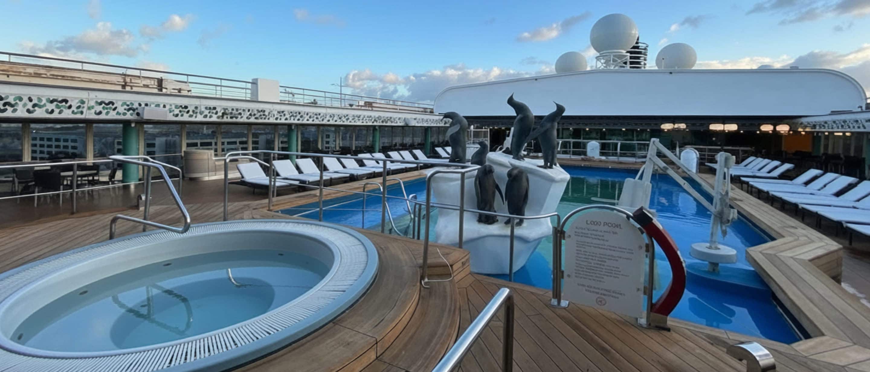 Pool and hot tub area on a Holland America cruise ship with lounge chairs and a central sculpture.