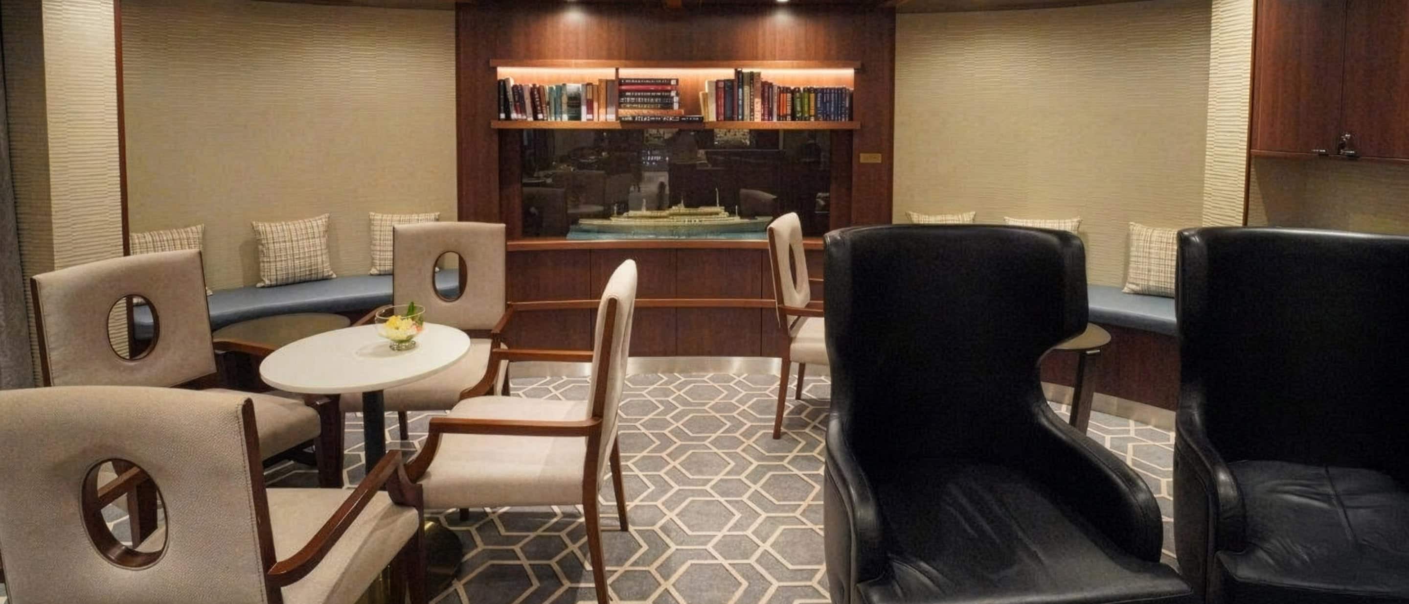 Lounge area aboard the Holland America Line with comfortable seating, a small table, and a bookshelf.