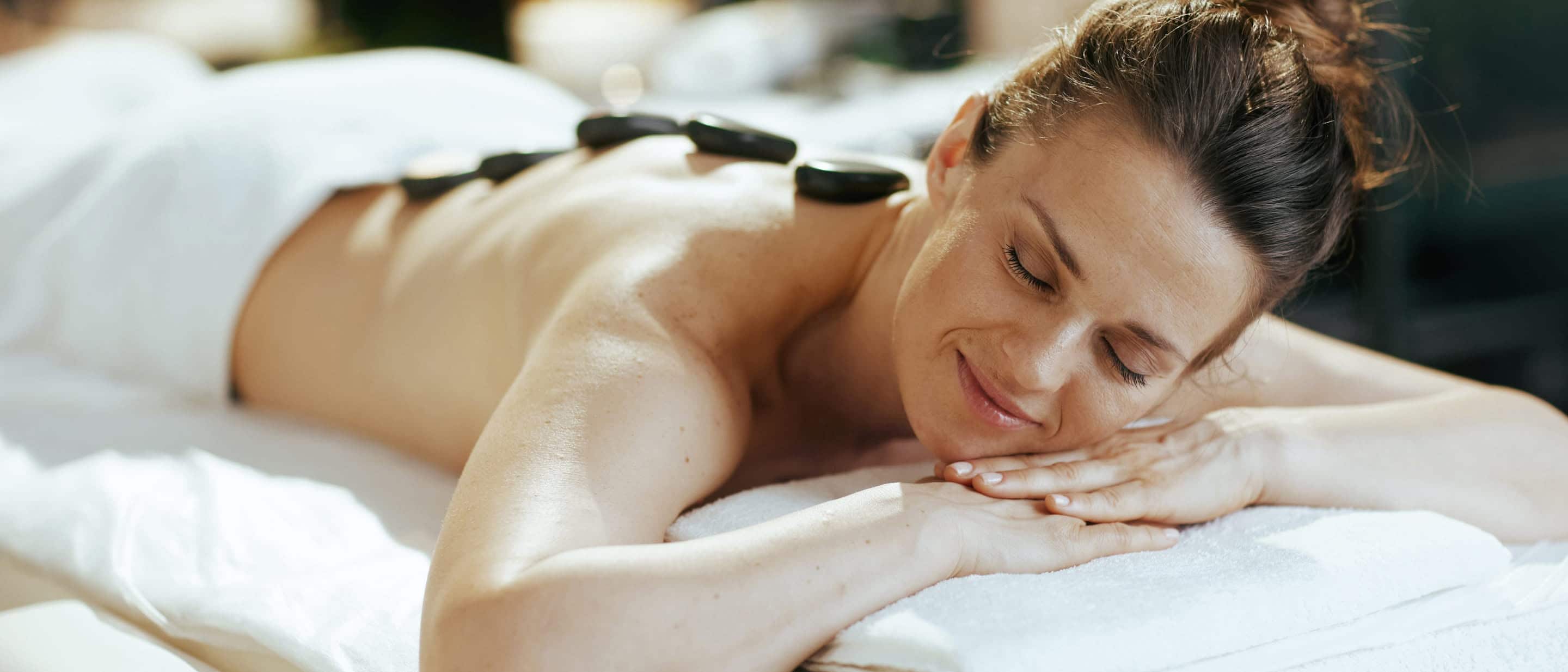 Person lying face down during a hot stone spa treatment with stones placed along the back on a massage table.