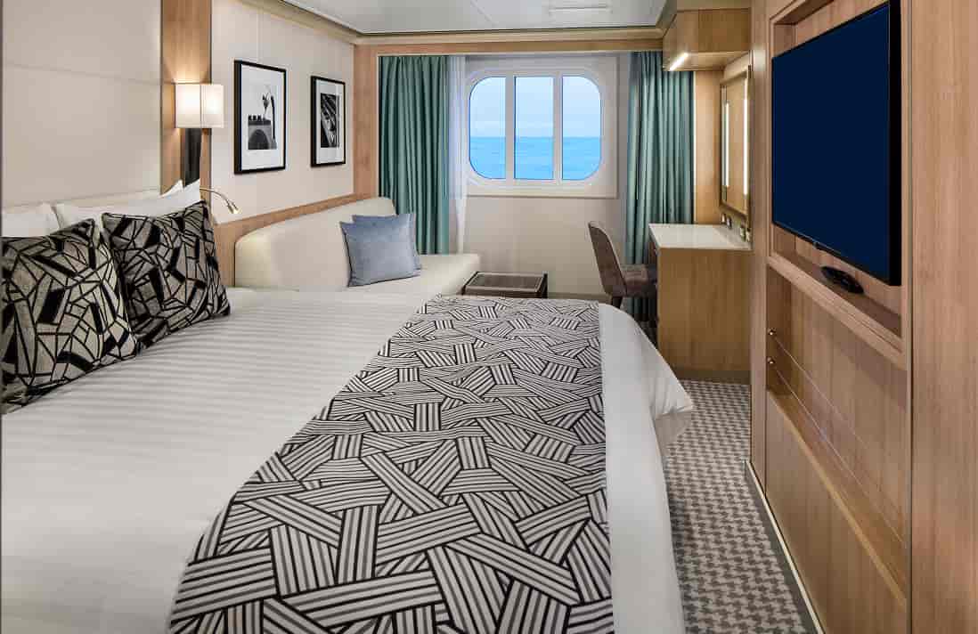 Family Ocean View stateroom with queen bed, wall-mounted TV, desk, sofa, and framed artwork on a Holland America cruise ship.