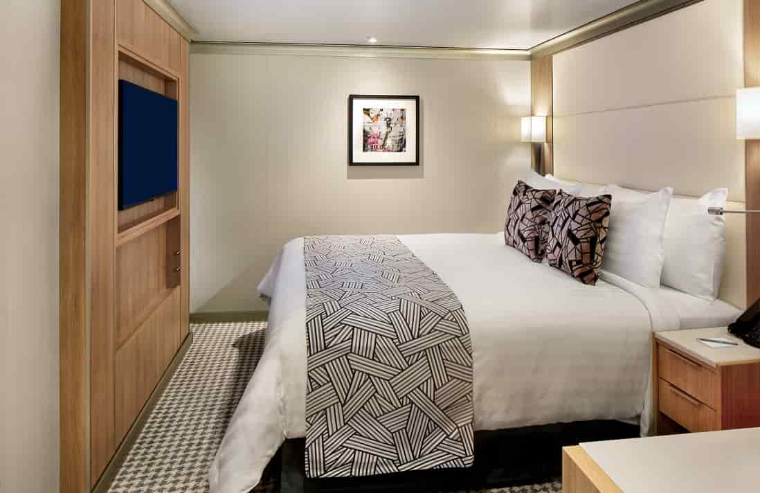 Inside stateroom with queen bed, wall-mounted TV and framed artwork on a Holland America cruise ship.