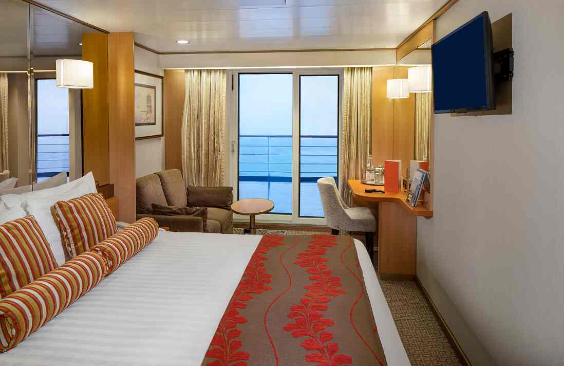 Lanai Verandah stateroom with queen bed, sofa, desk, and sliding doors to balcony on Holland America cruise ship.