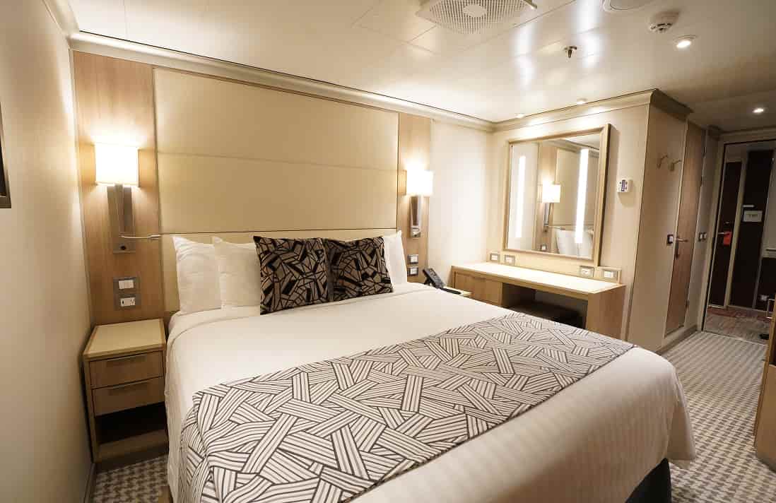 Large inside stateroom with queen bed, bedside lamps, and modern décor on Holland America cruise ship.