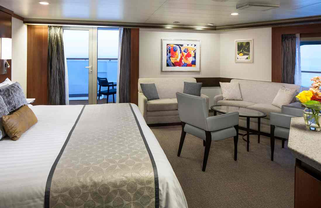 Neptune Suite with king bed, sitting area, sofa and balcony overlooking the ocean on a Holland America cruise ship.